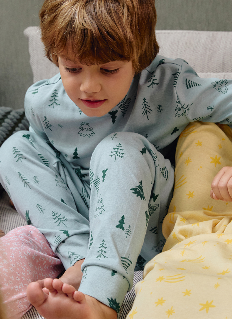 Dječak sjedi na krevetu u zelenoj pidžami na dug rukav sa motivom jelkica