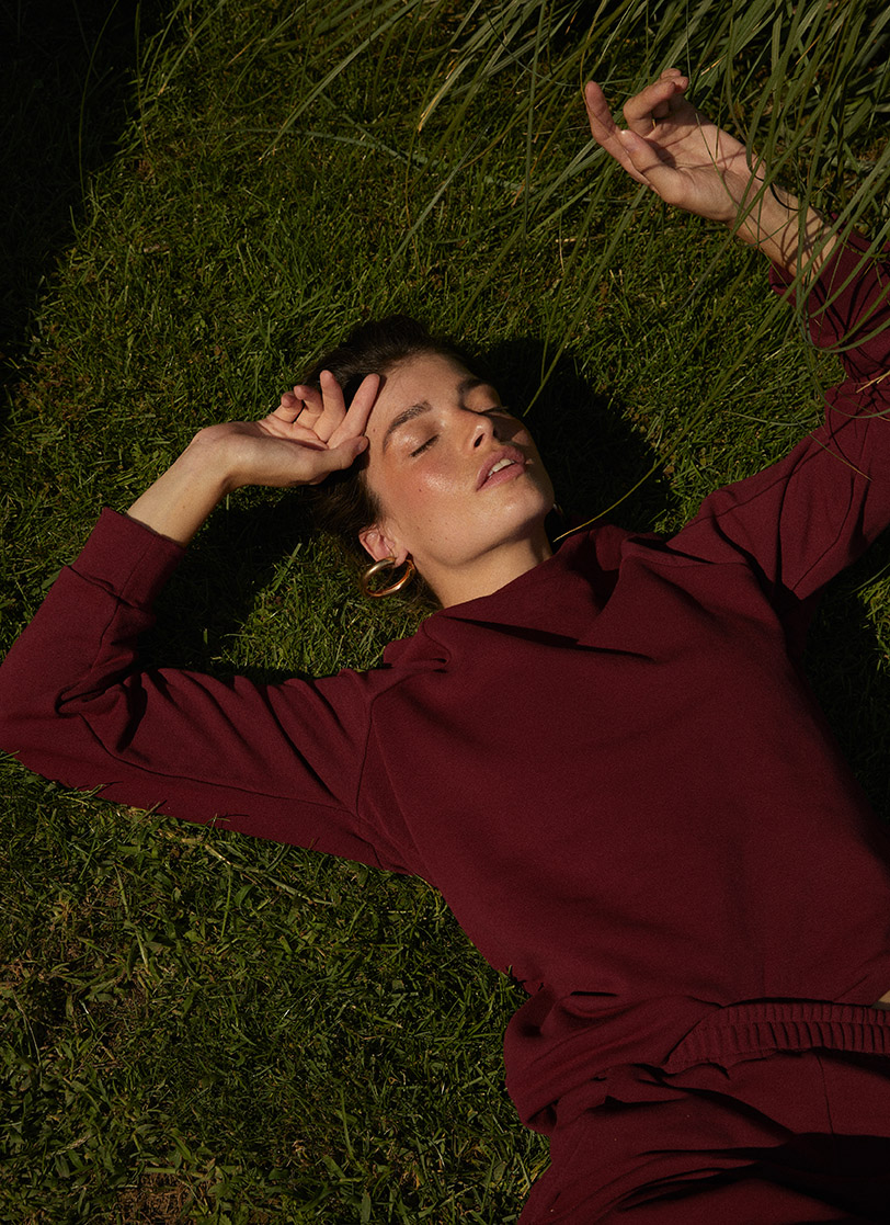 Žena leži na travi i  nosi bordi dukser .