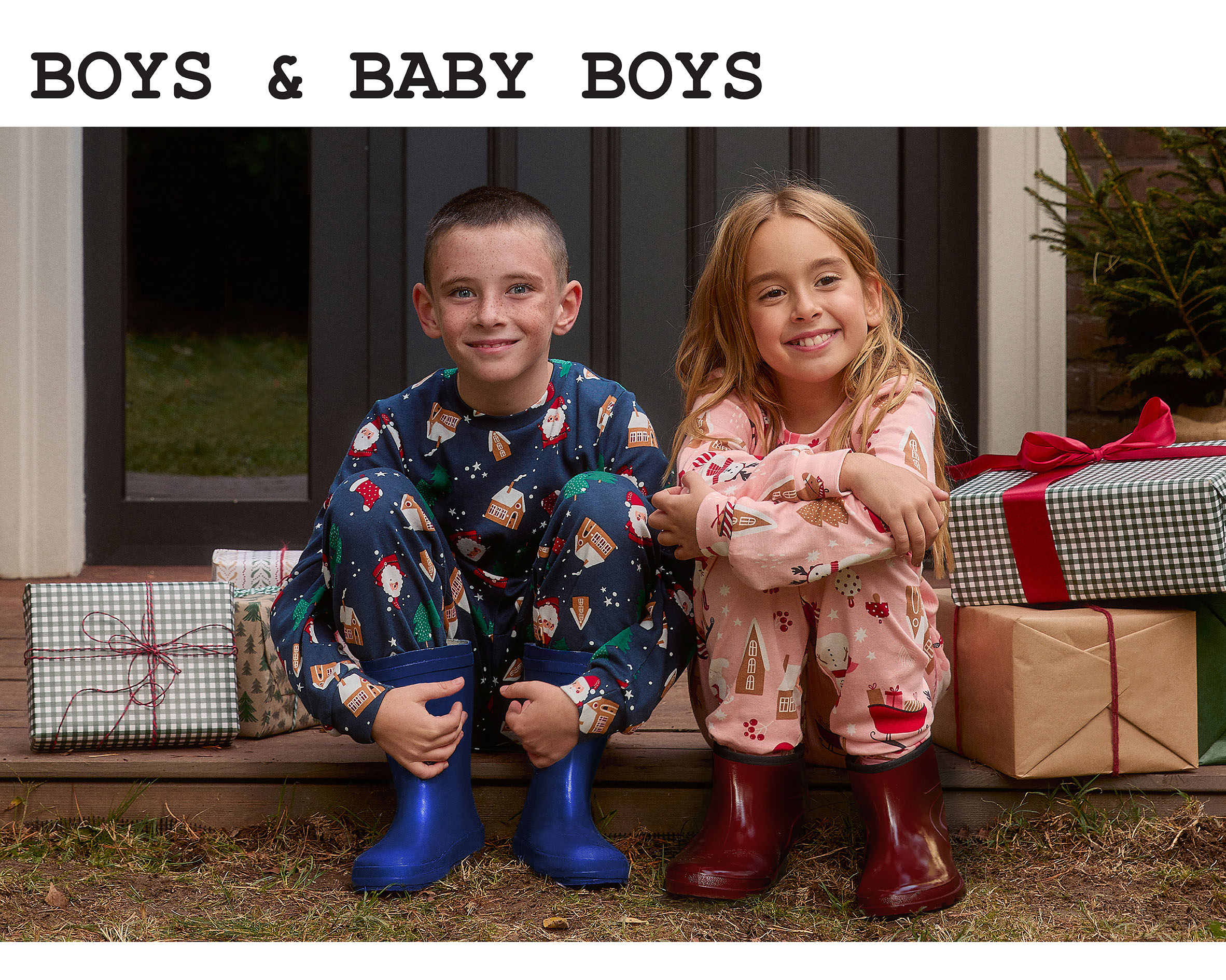 Dječak  i djevojčica sede pored poklona u novogodišnjim pidžamama