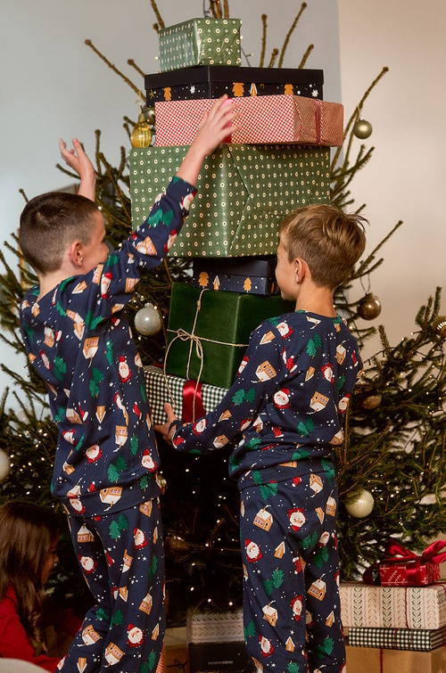 Dječaci stoje pored jelke i poklona u novogodišnjim pidžamama