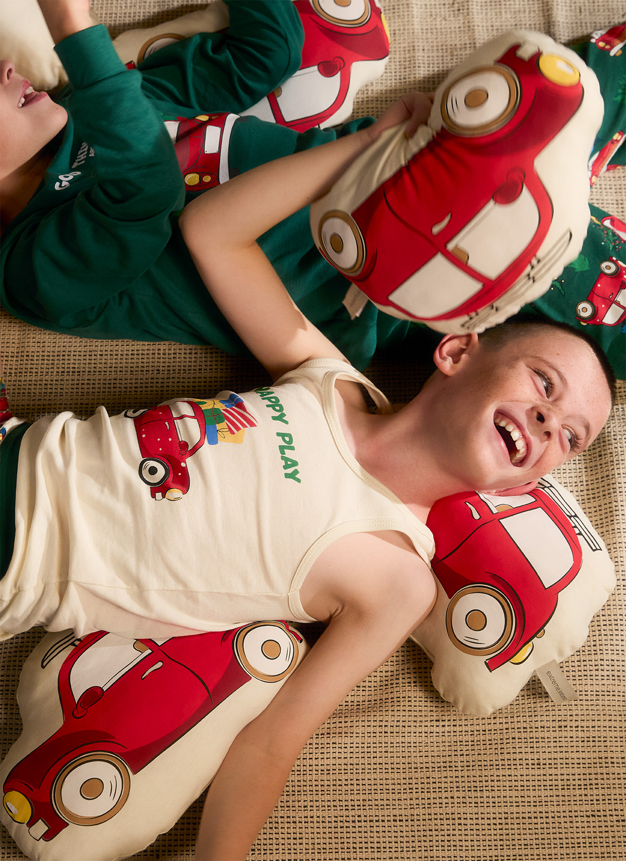 Dječaci leže na podu obučeni u novogodišnje artikle  i drze novogodišnji jastuk u obliku auta