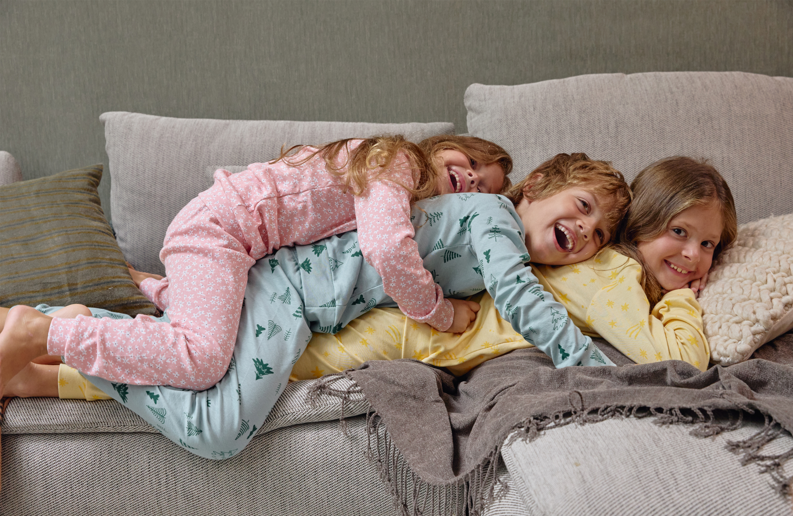 Dječak i dve djevojčice leže na krevetu u šarenim pidžamama